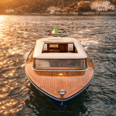 Wooden boat with Italian flag on a lake at sunset, with hillside buildings in the background.