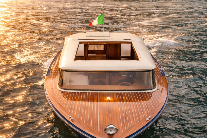 Wooden boat with Italian flag on a lake at sunset, with hillside buildings in the background.
