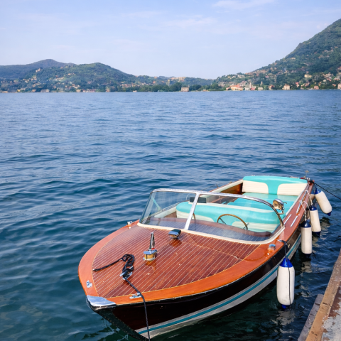 Wooden speedboat docked on a calm lake with hills in the background.