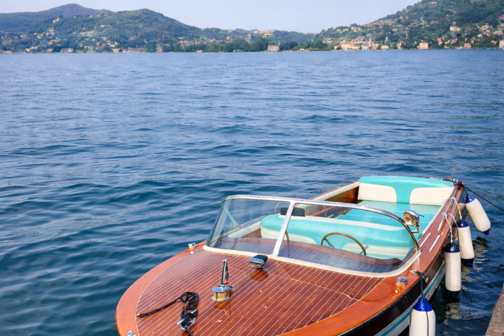 Wooden speedboat docked on a calm lake with hills in the background.