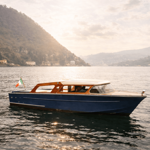 Wooden boat with Italian flag on a lake with mountains in the background, under a cloudy sky.