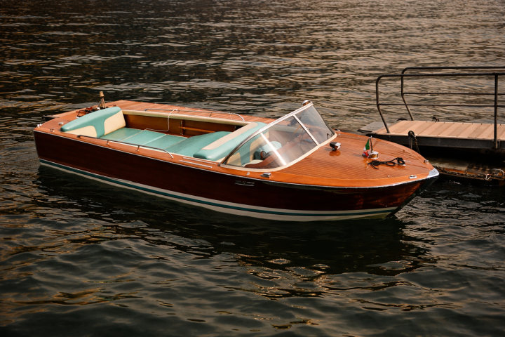 Wooden motorboat with teal seats docked beside a pier on calm water.