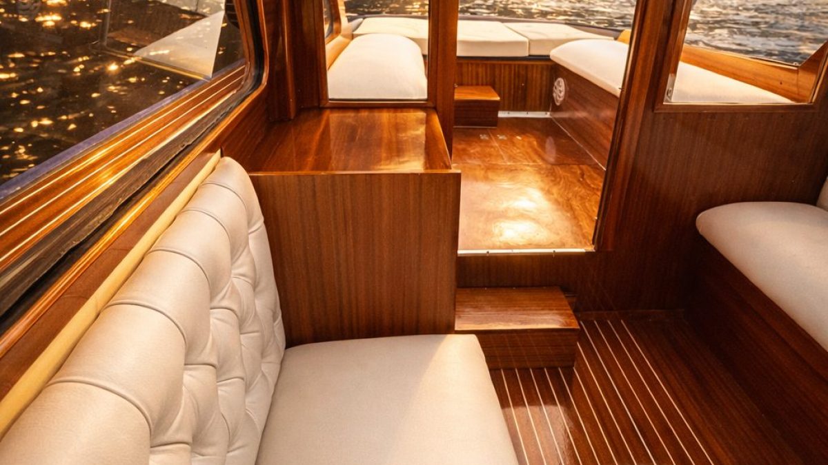 Luxurious wooden boat interior with white cushions and lake view at sunset.