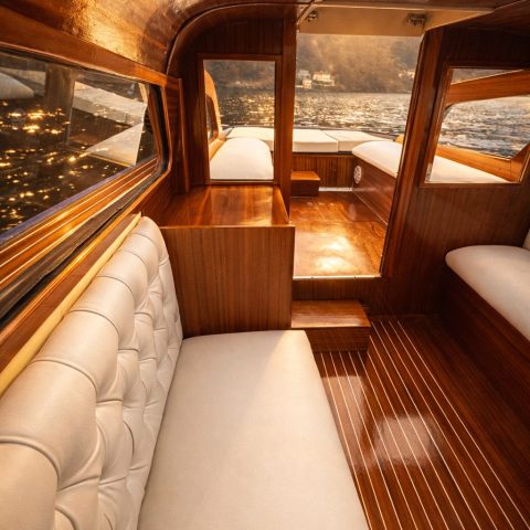 Luxurious wooden boat interior with white cushions and lake view at sunset.