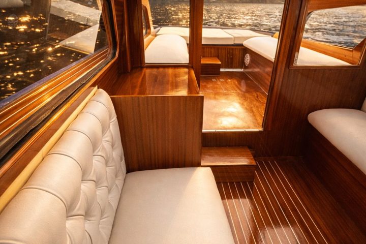 Luxurious wooden boat interior with white cushions and lake view at sunset.