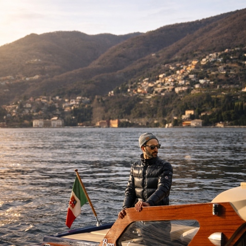 Man in sunglasses on a boat at sunset with mountains in the background.