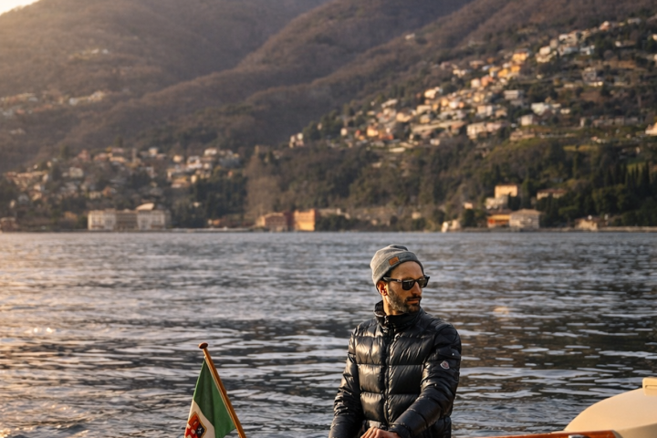 Man in sunglasses on a boat at sunset with mountains in the background.