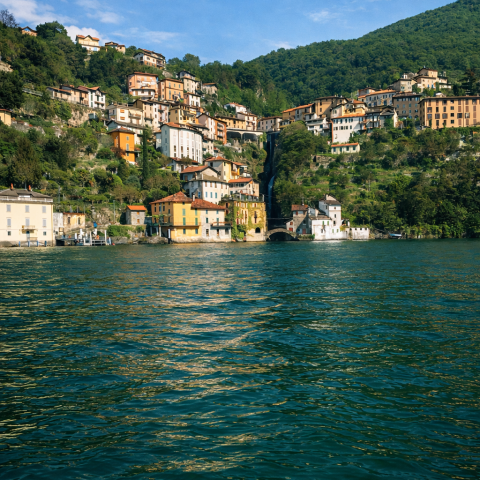 Hillside village with colorful houses overlooking a large, calm body of water.
