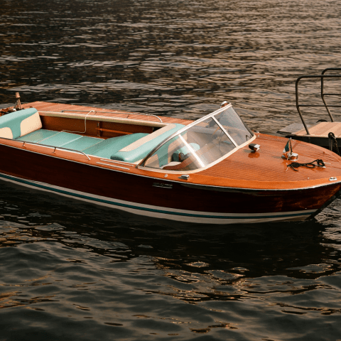 A vintage wooden boat with aqua seats docked on calm water.