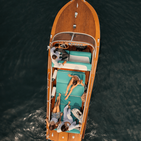 Aerial view of people relaxing on a wooden boat with teal seats in calm water.