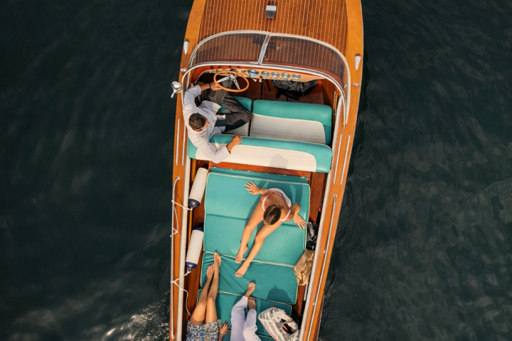 Aerial view of people relaxing on a wooden boat with teal seats in calm water.