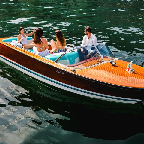 People relaxing on a wooden speedboat in calm water, sunny day.