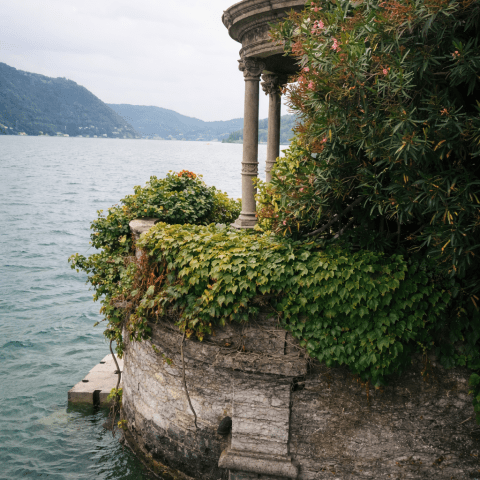 Stone pavilion with ivy near lake, hills in background.