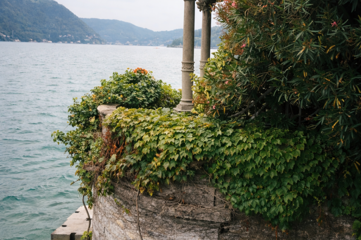 Stone pavilion with ivy near lake, hills in background.