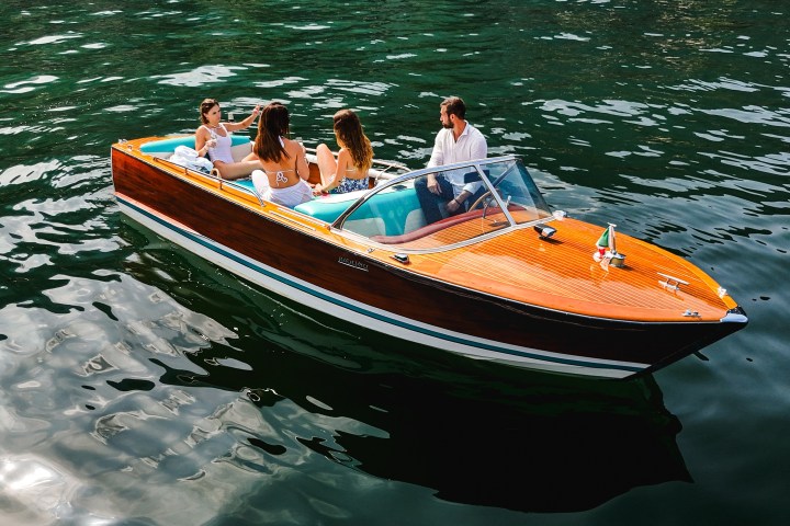 Four people sit in a wooden motorboat on calm, green water.