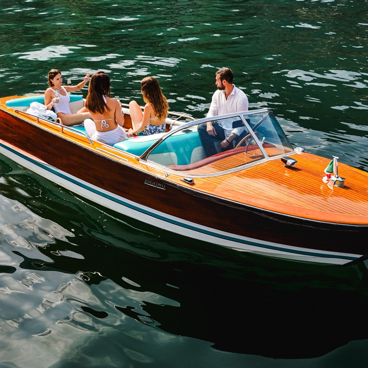 Four people sit in a wooden motorboat on calm, green water.